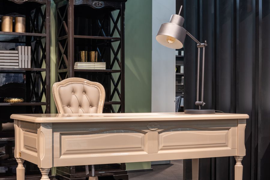 A book-lined study with a wooden table, chair and warm lamp light