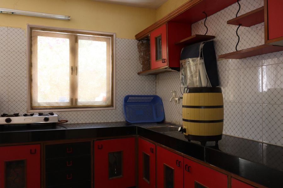 A bright Indian kitchen with red cabinets and morning window light