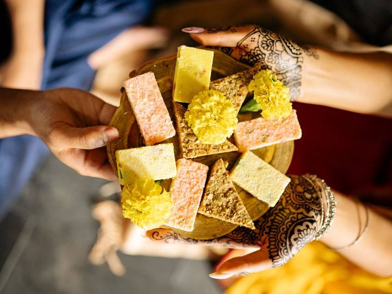 Hands with mehendi holding a plate of assorted Indian sweets