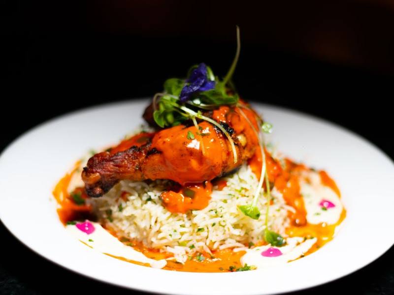 Tandoori chicken plated over rice with sauces on a white plate