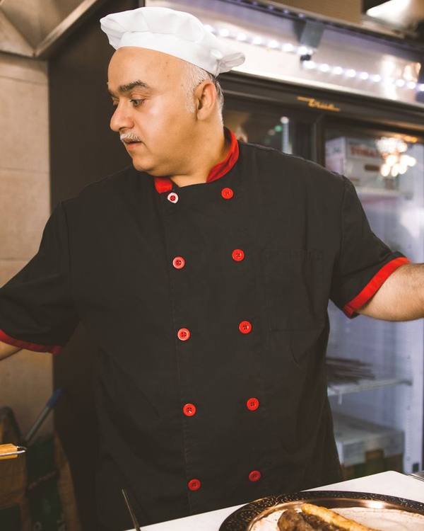 Indian chef in a black chef's coat working at a kitchen counter