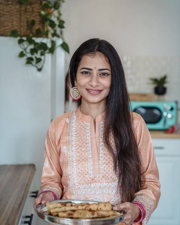 Smiling Indian woman in a pink kurta holding a tray of food