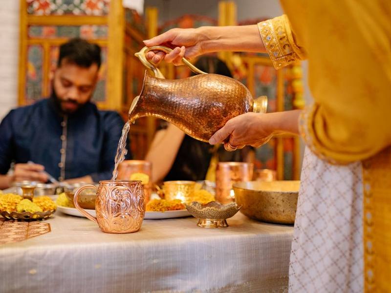 Server pouring water from a brass jug at a traditional Indian dining table