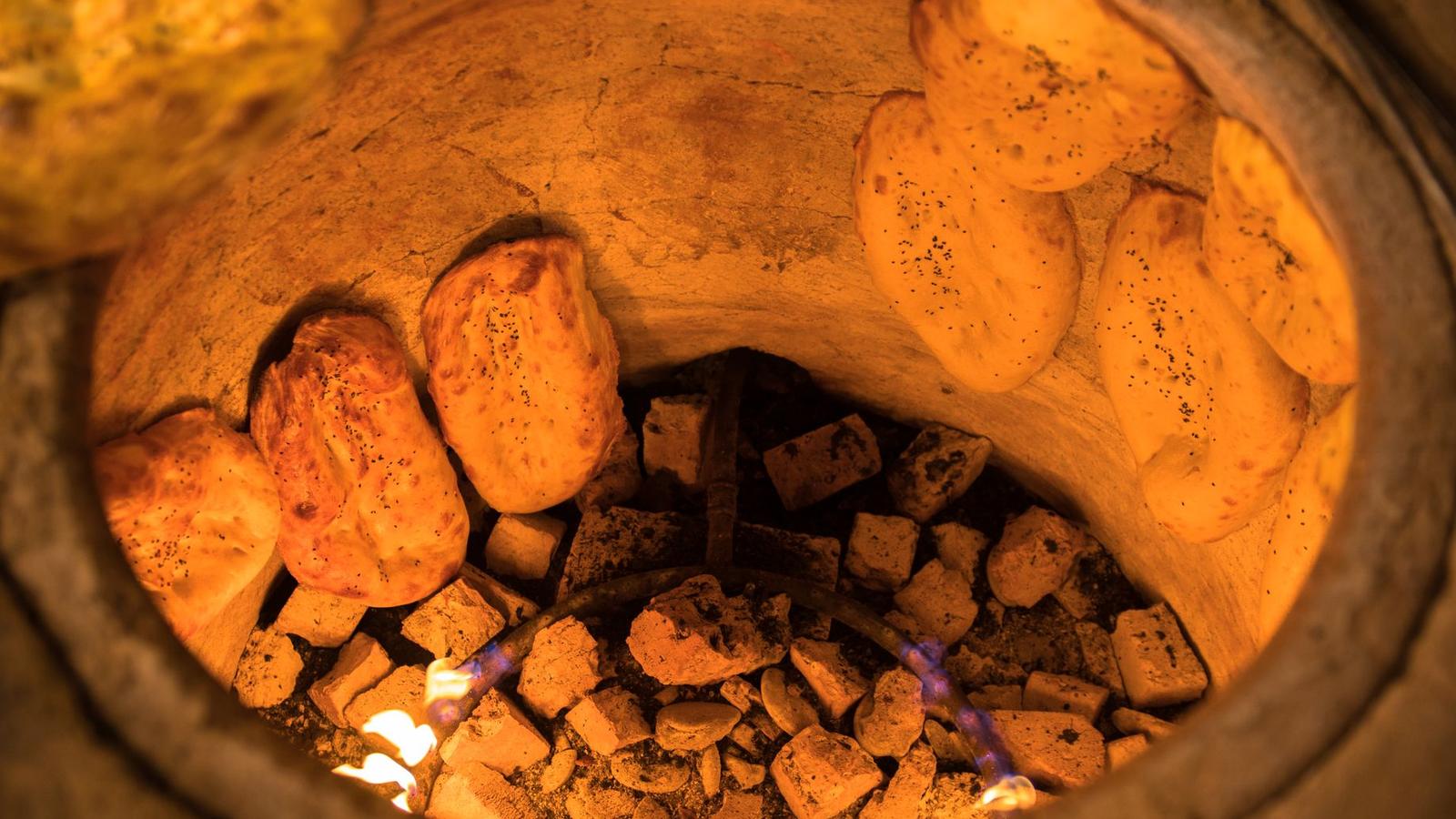 Naan breads baking against the glowing charcoal wall of a clay tandoor