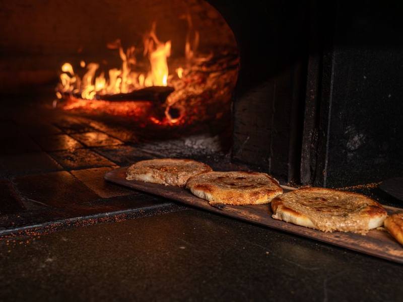 Flatbreads baking beside a roaring wood fire in a clay oven