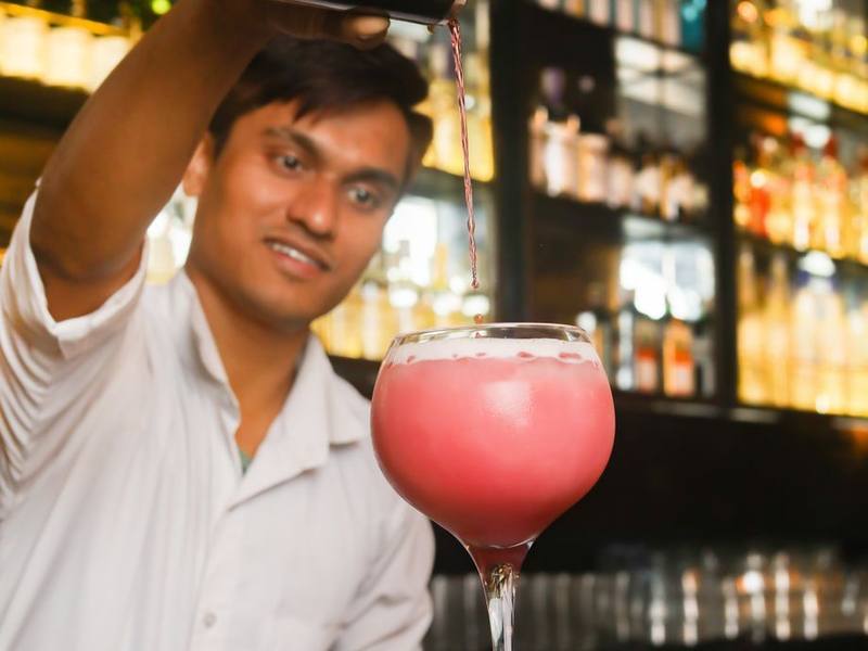 Indian bartender shaking a cocktail with a pink drink in the foreground