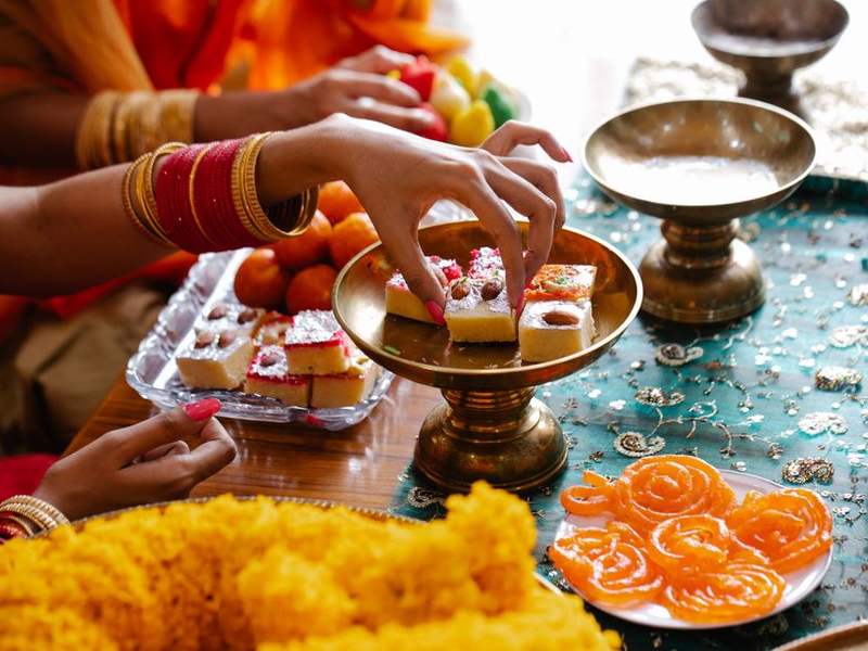 Hands reaching for sweets and jalebi on brass stands at a festive table