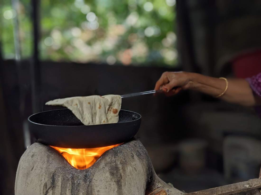 A hand flipping a roti on a cast-iron tawa over a wood fire
