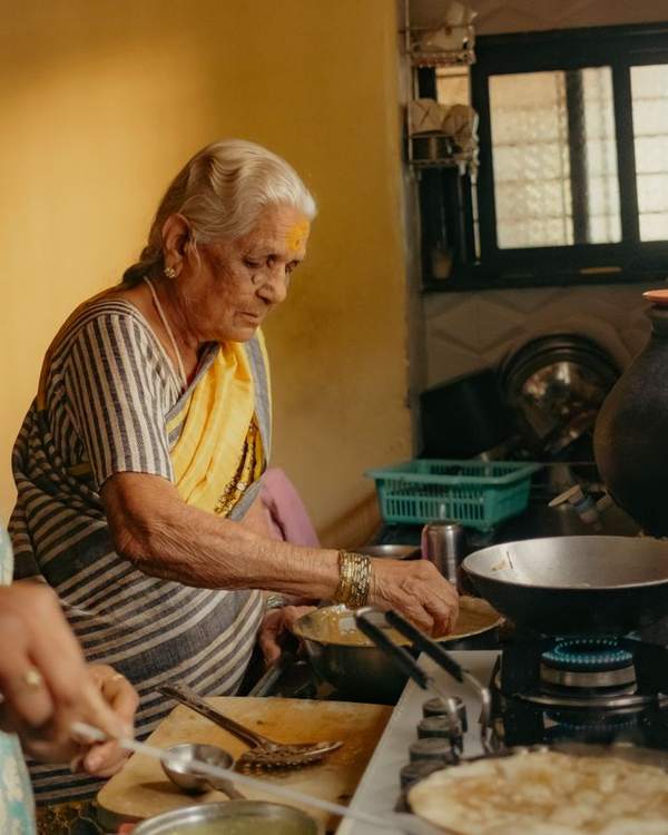 Elderly Indian woman in a saree cooking at a home kitchen stove