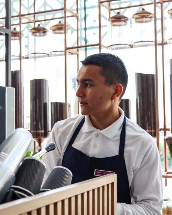 Young Indian man in a dark apron working behind a café counter