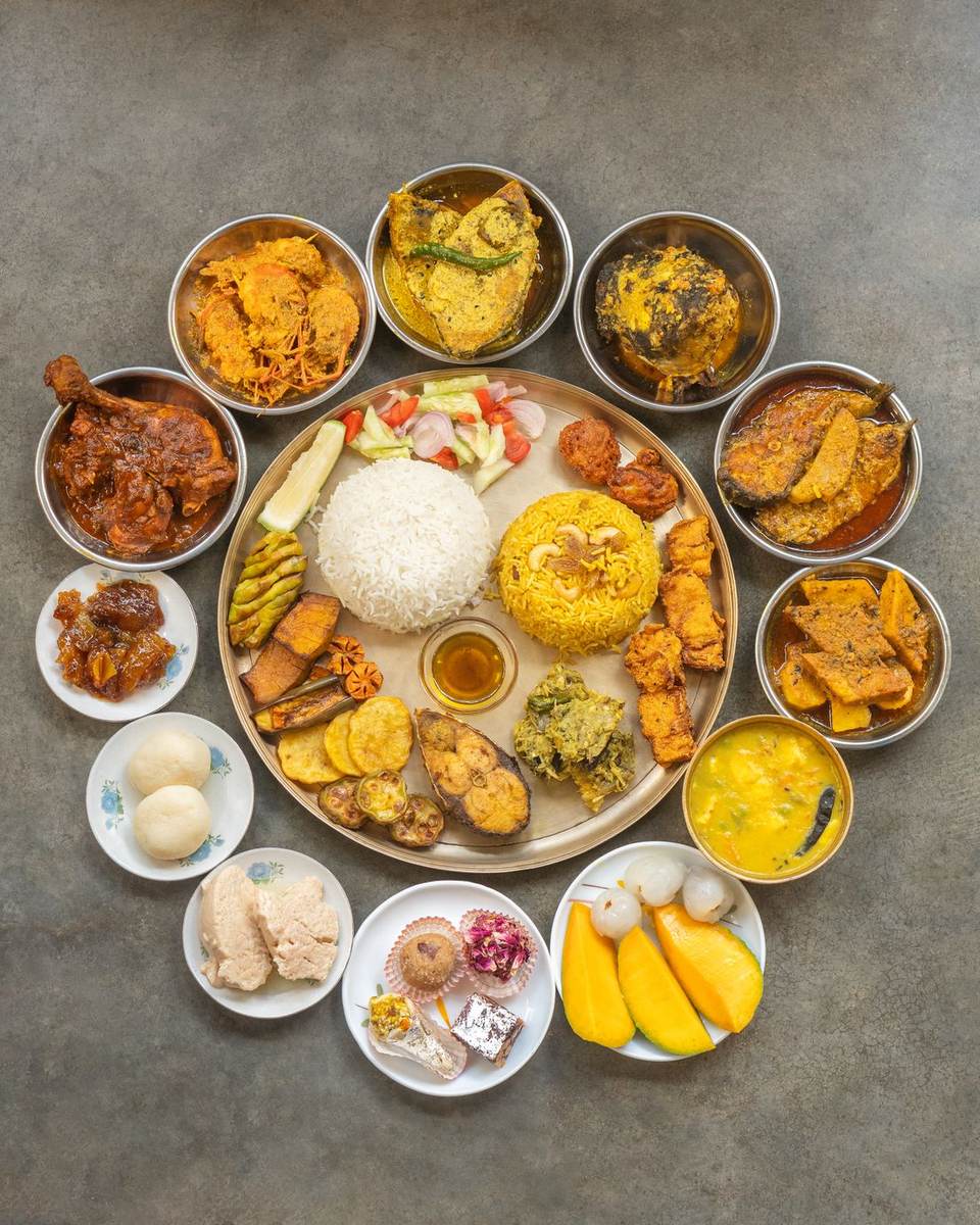 A full Bengali thali of rice, dal, bhaja, fish curry, mutton and mishti in small brass bowls