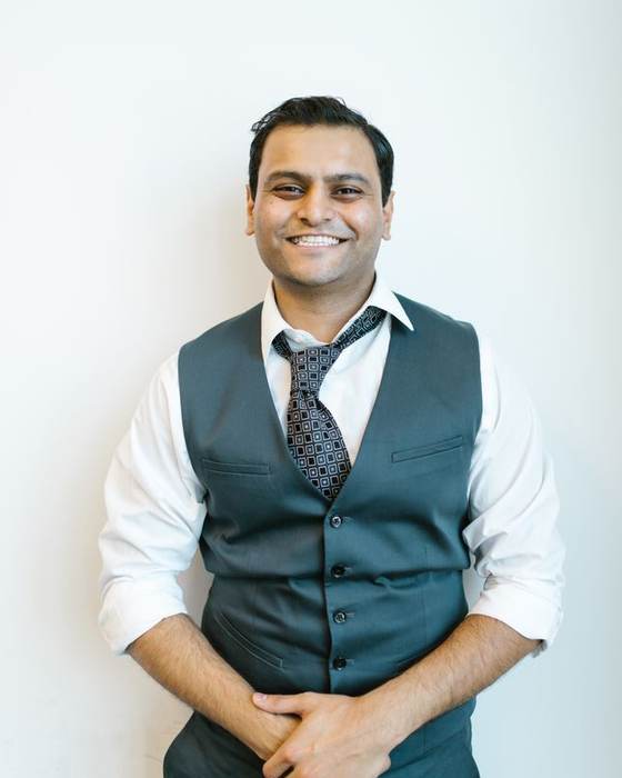 Smiling Indian man in a white shirt and grey waistcoat with hands clasped
