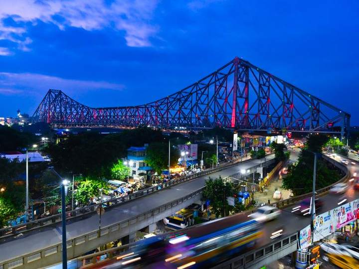 Howrah Bridge lit up at dusk with traffic trails on the road below