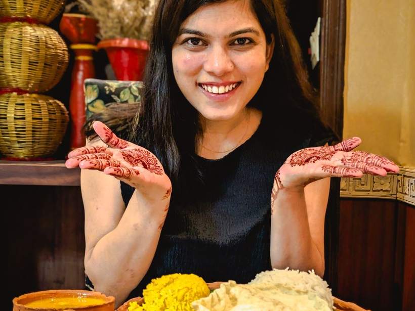A smiling Indian woman in a black top presenting a large Bengali thali at a table