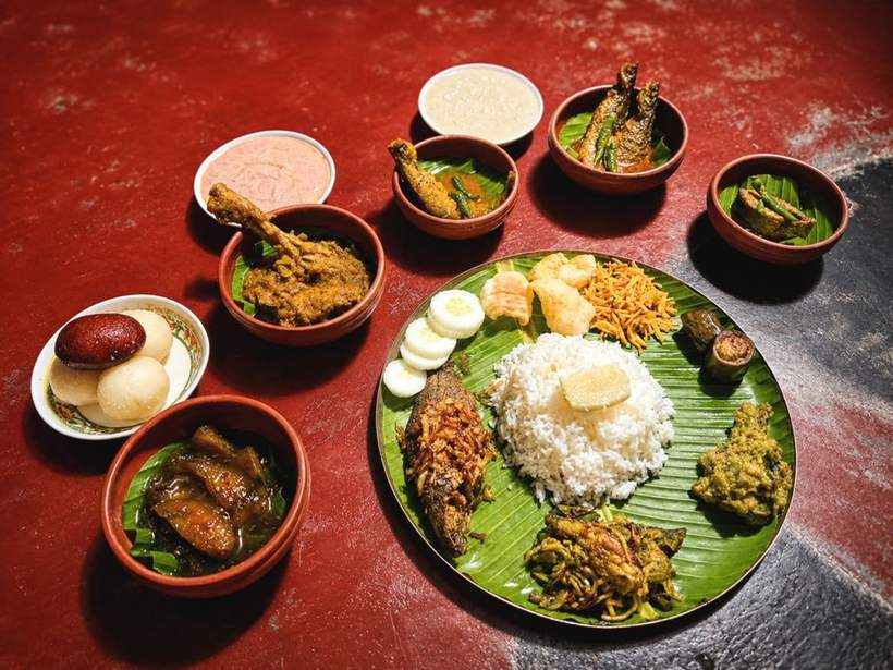 A Bengali fish thali on a banana leaf with rice and several bowls set on a red cloth