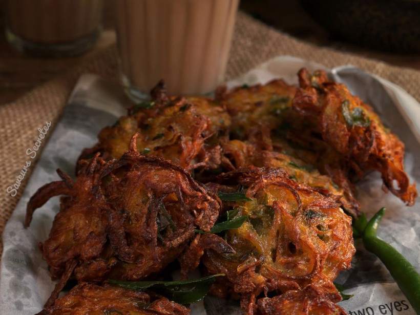 A plate of fritters and a glass of milky tea on a dark wooden table
