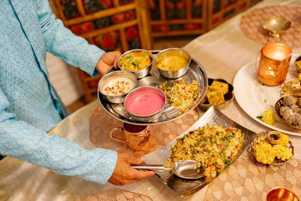A host serving a traditional Indian thali to guests at a festive gathering