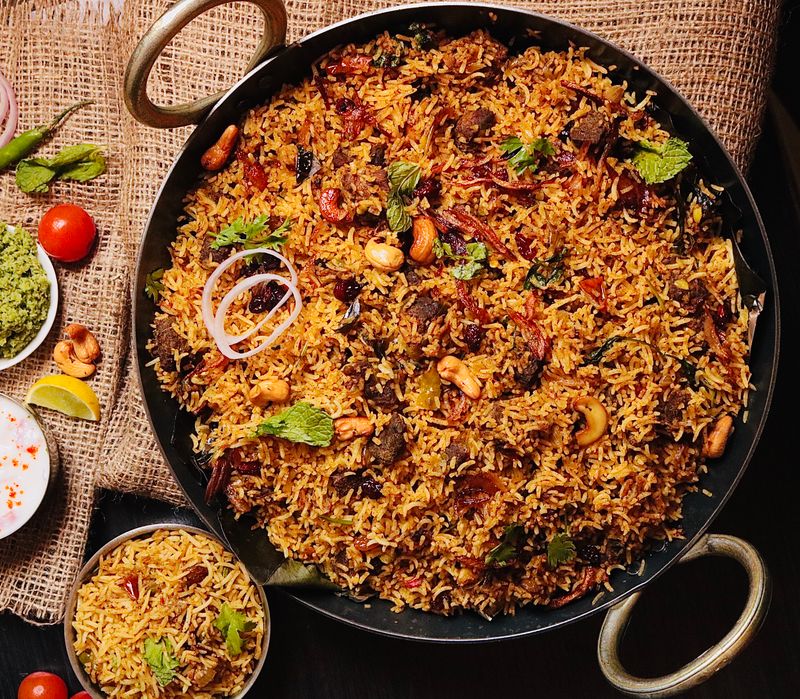 Saffron dum biryani garnished with cashews and herbs in a cooking handi