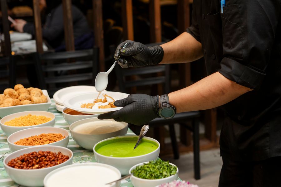 A chef assembling traditional Indian chaat with toppings and chutneys at a live counter