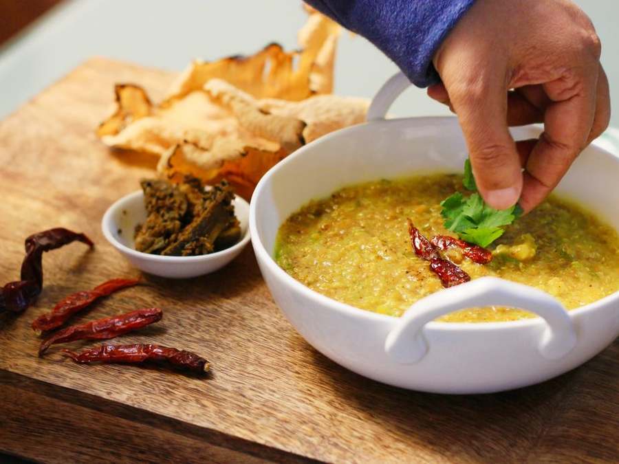 Hand garnishing a bowl of haleem with coriander beside flatbreads