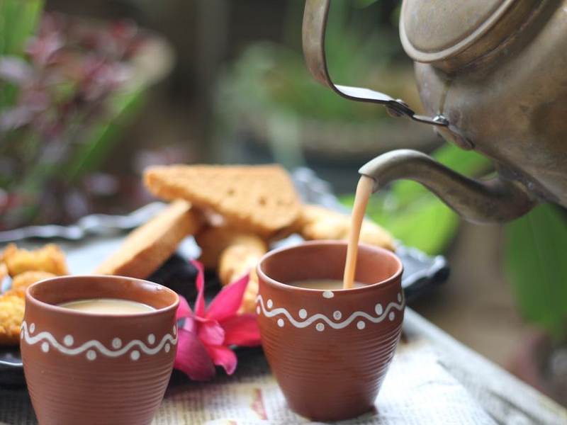 Chai being poured from a kettle into clay cups beside rusks