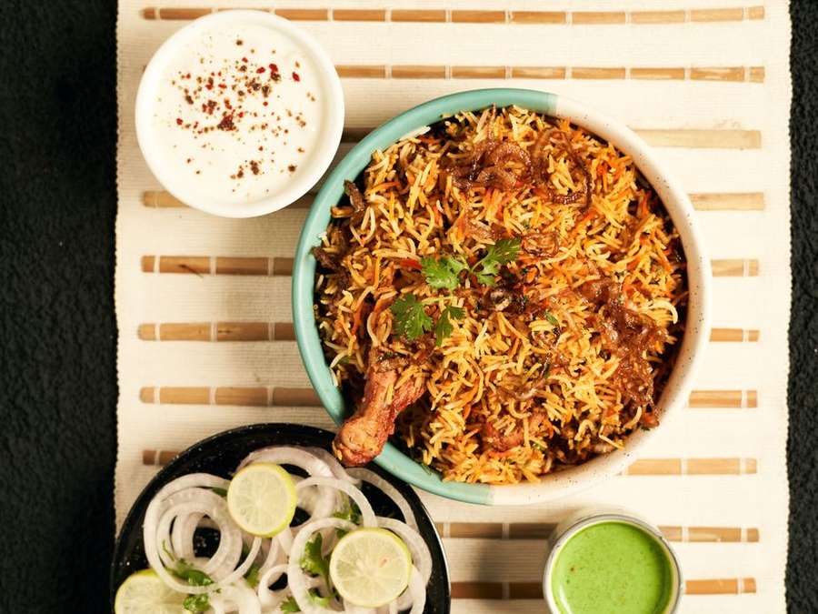 Overhead view of chicken biryani served with raita, onion rings and chutney