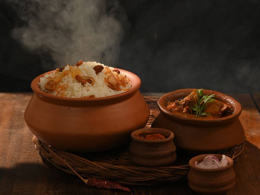 Clay biryani pot steaming on a wooden table with smaller pots beside it
