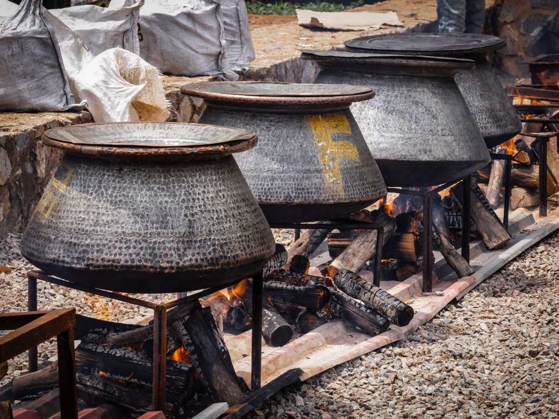 Large iron degs steaming over wood fires in an open-air kitchen