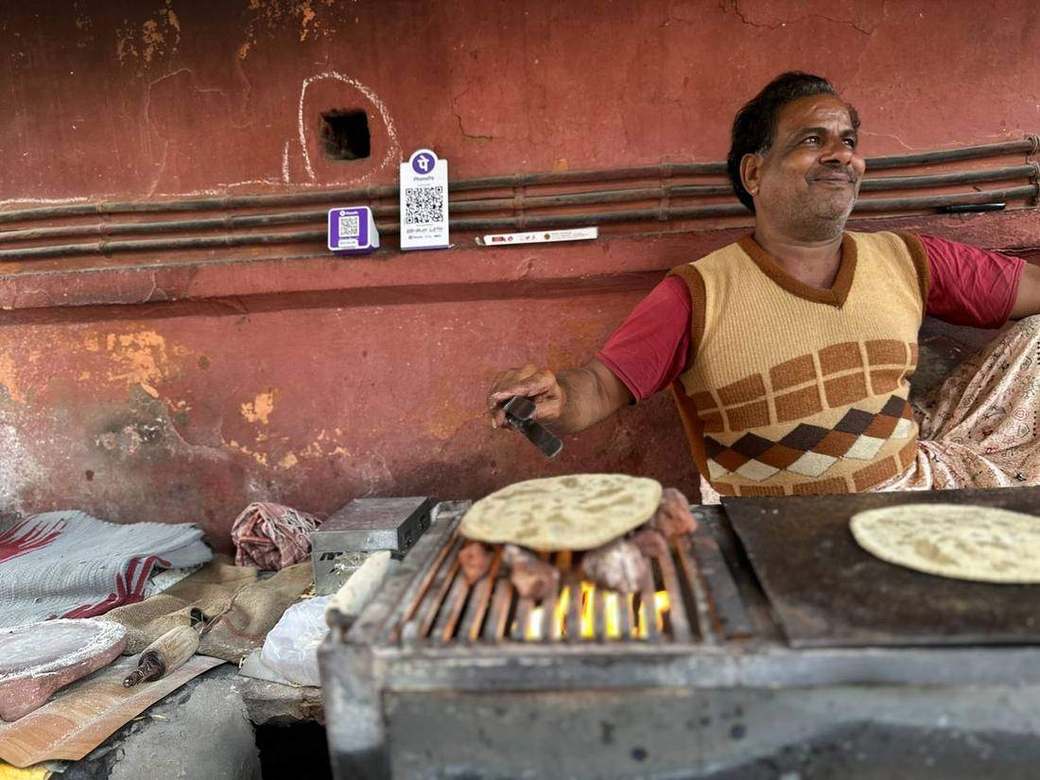 Cook rolling rotis at a red-walled dhaba counter with a tawa full of rotis