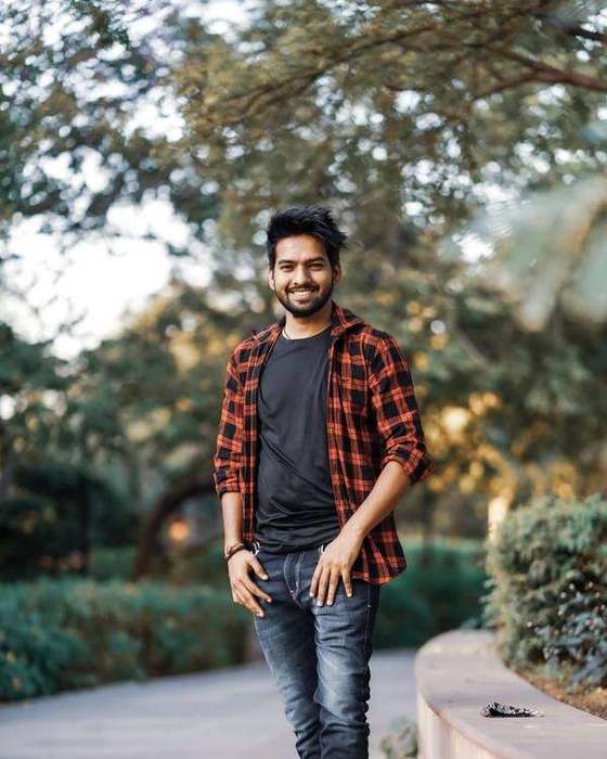 Young Indian man in a checked shirt standing under a tree