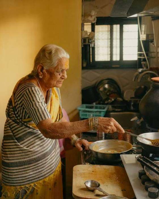 Older Indian woman cooking rotis on a tawa by a sunlit window