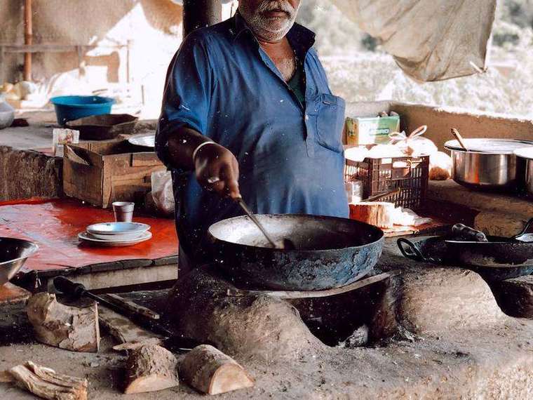 Cook stirring a large iron kadhai over a wood fire at the dhaba