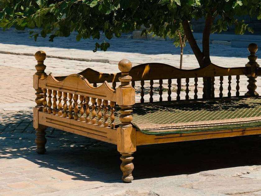 Wooden charpai under a large shady tree in a sunlit courtyard