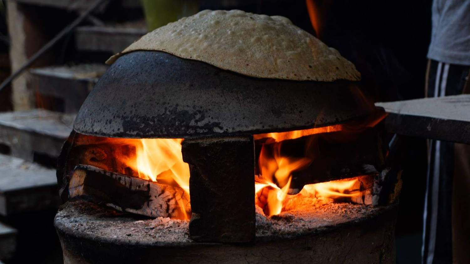 A roti puffing over the open flame of a clay tandoor at night