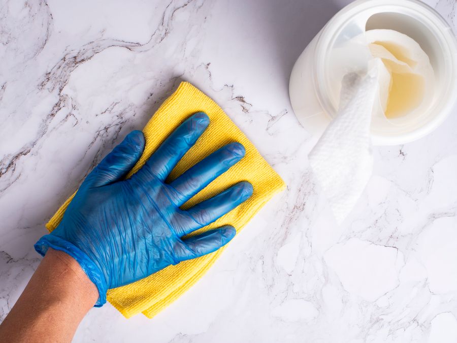 A gloved hand polishing a marble countertop with a yellow cloth