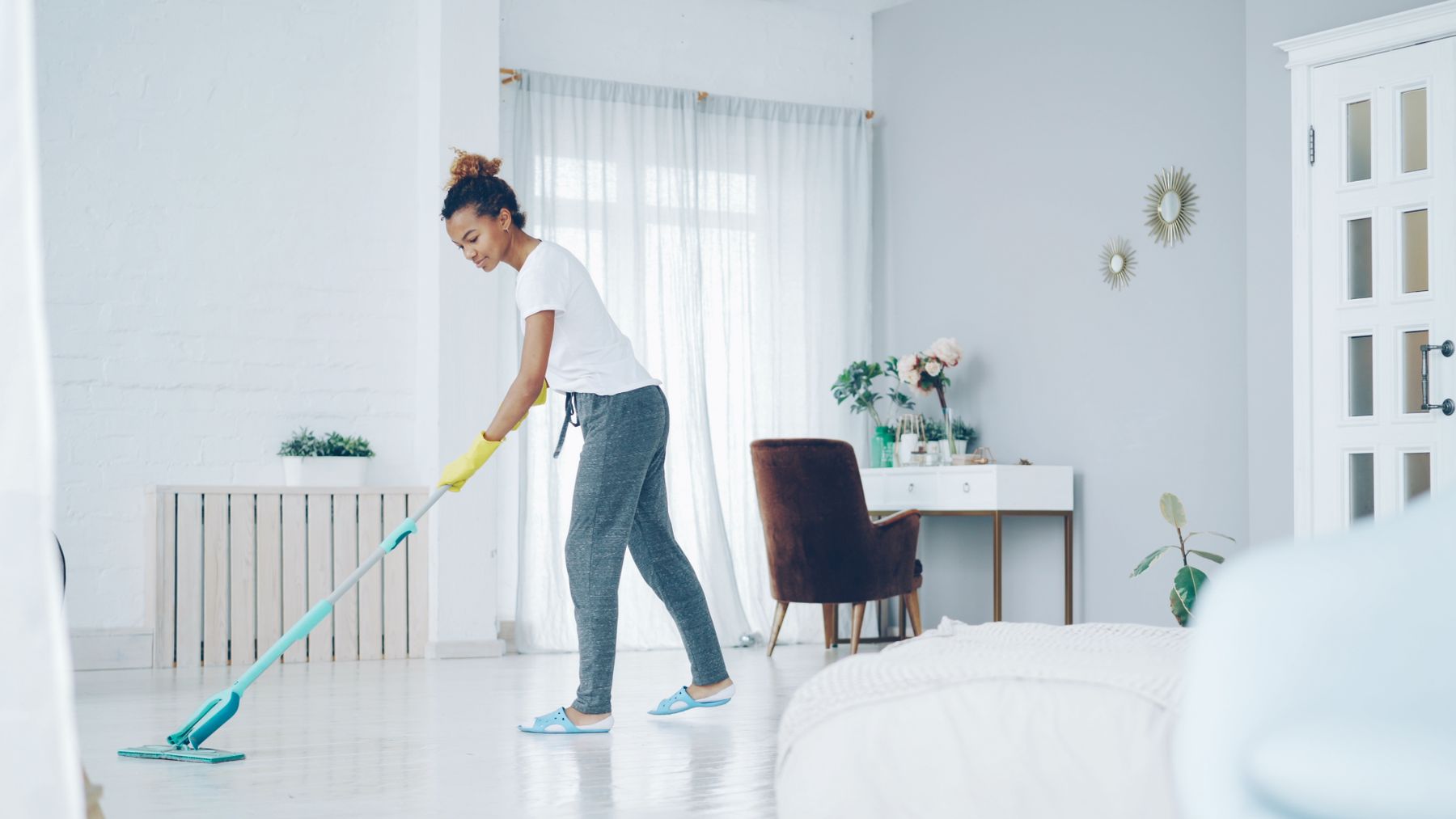 A cleaner mopping the gleaming white floor of a bright, airy bedroom