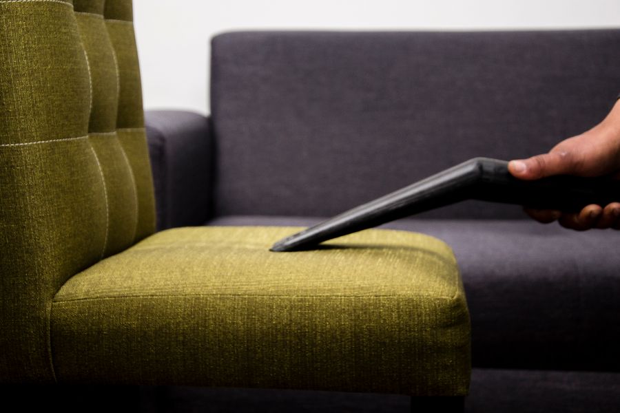 An upholstery tool deep-cleaning the seat of an olive-green sofa