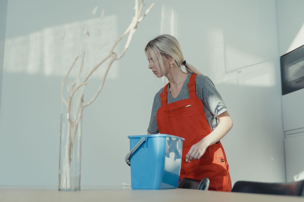 A Dhavala professional in uniform wiping down a bright white kitchen beside a blue bucket
