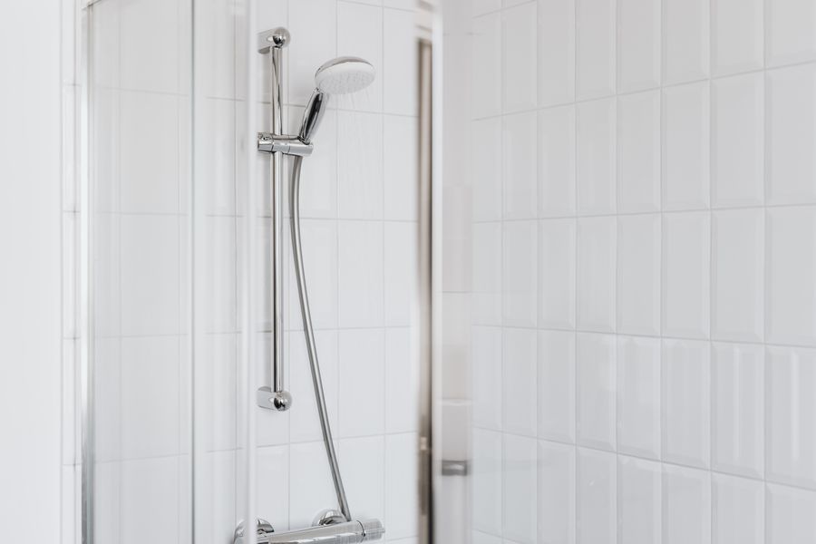A chrome shower head against sparkling white tiles after a Dhavala descale