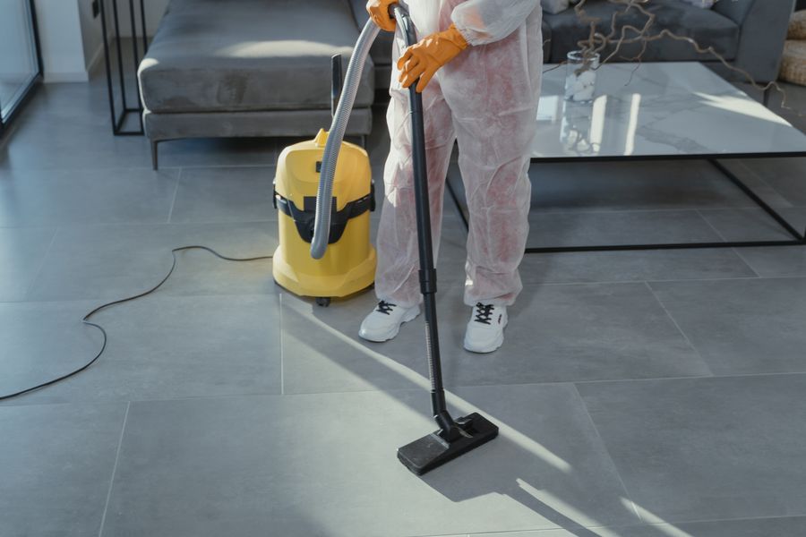 A professional cleaner machine-vacuuming the tiled floor of a modern living room