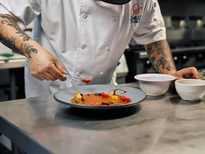 Chef plating a dish on a dark plate at the pass