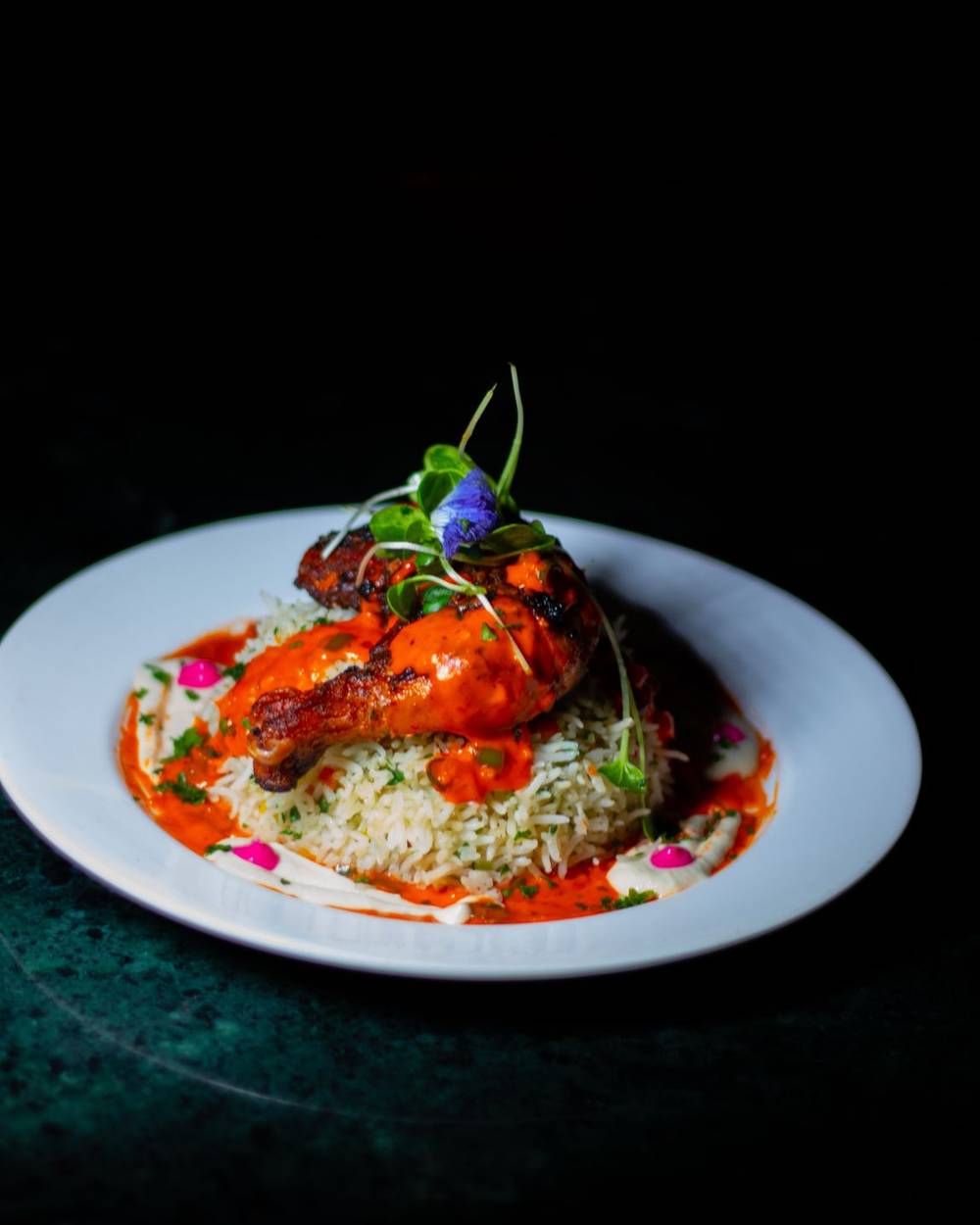 Chef's hands placing a garnish on a dark fine-dining plate under a single light