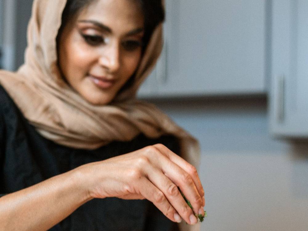 Indian woman chef in a dark apron plating a dish at a kitchen counter