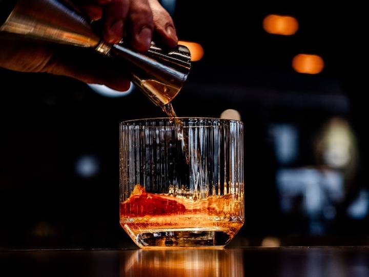Bartender pouring a drink over ice at a dimly lit bar