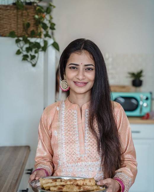 Indian woman chef holding a plated dish in a bright kitchen