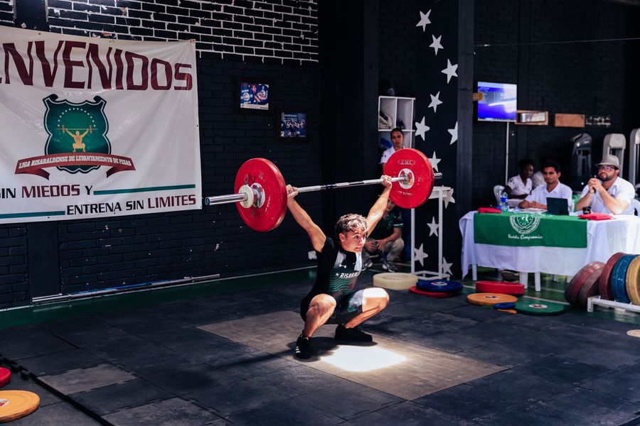 A weightlifter locking out a snatch overhead on a platform
