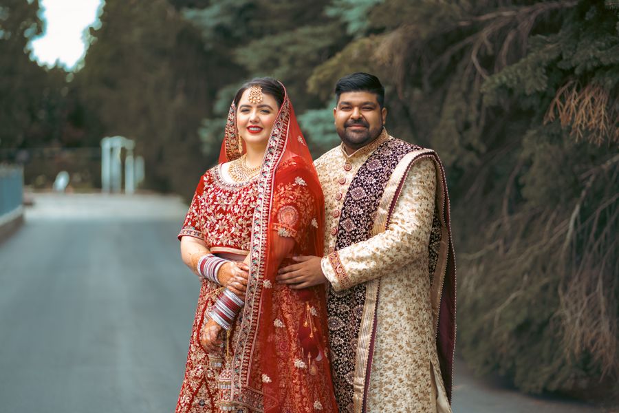 A couple in vibrant traditional Indian wedding outfits posing together outdoors