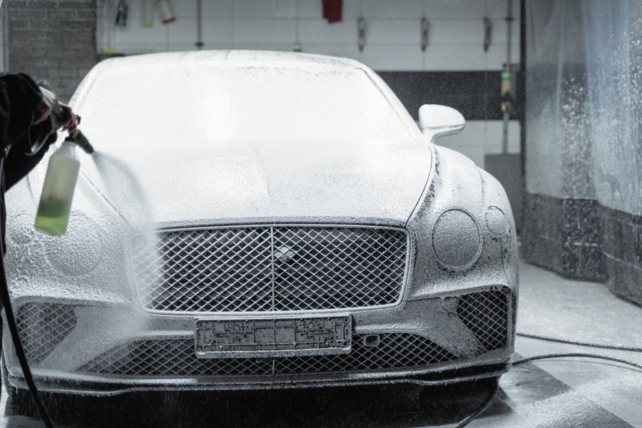 A luxury car covered in thick snow foam during a hand wash in the bay