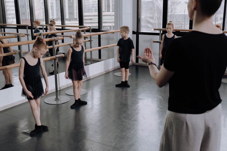 Young children practising a dance routine in a bright studio with their instructor