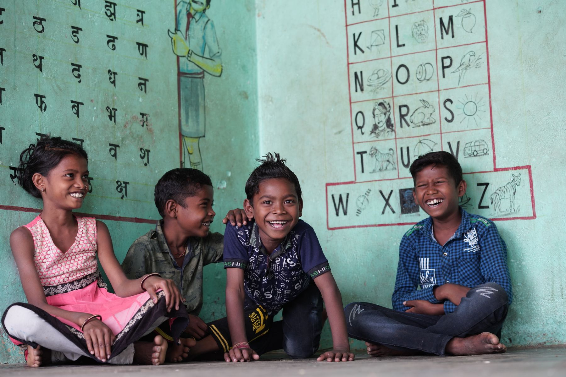 A group of happy Indian children laughing together in a colourful classroom at Gubbara